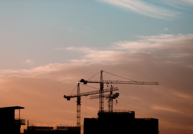 建設業の夏季休工を解説する記事のアイキャッチ。夕暮れの建設現場とクレーンのイメージ